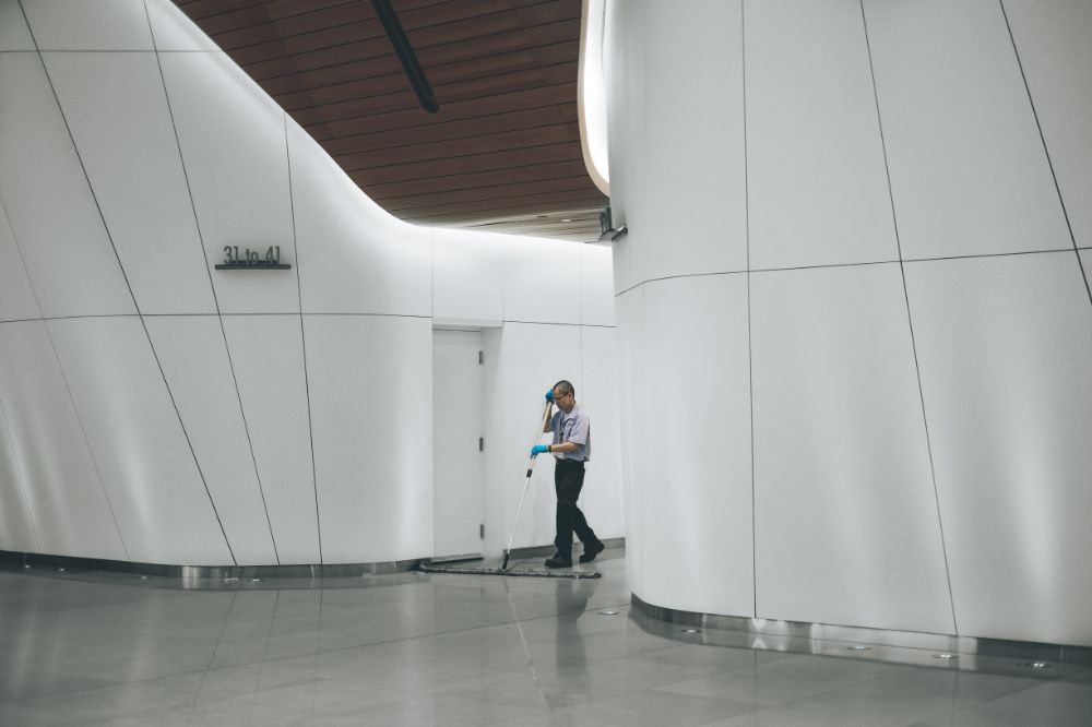 Male cleaner sweeping office floor with large broom