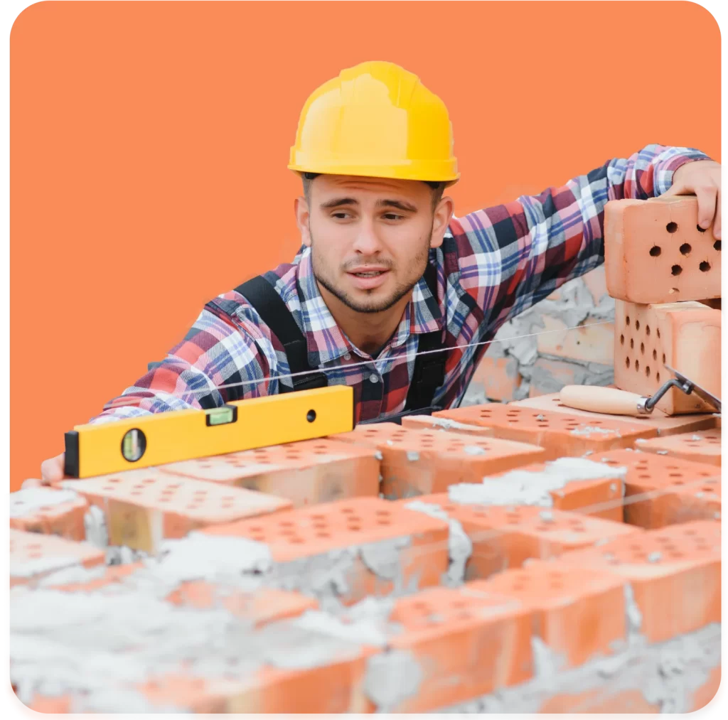 A construction worker in a yellow hard hat and plaid shirt uses a level tool to align bricks on an orange background, demonstrating the precision and safety practices essential for Bricklayers Insurance.