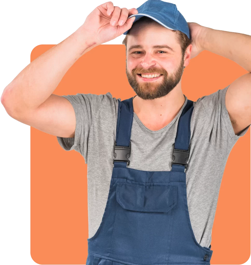 A bearded man in a gray t-shirt and blue overalls smiles while adjusting his blue cap against an orange background, confident and carefree thanks to his Dry Hire Insurance.