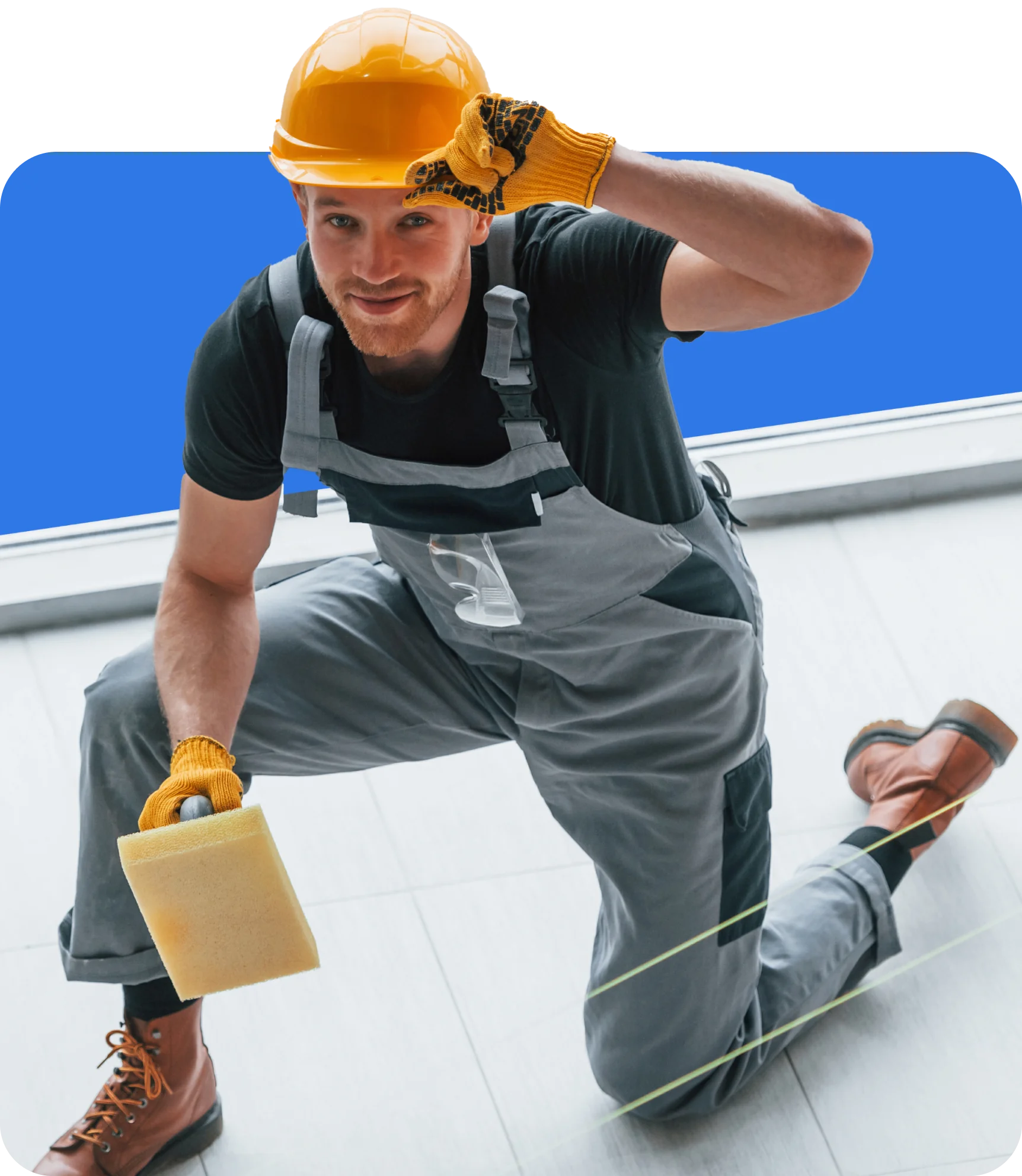 A construction worker wearing a yellow hard hat, gloves, and gray overalls is kneeling and holding a sponge—an ideal candidate for Tilers Insurance.