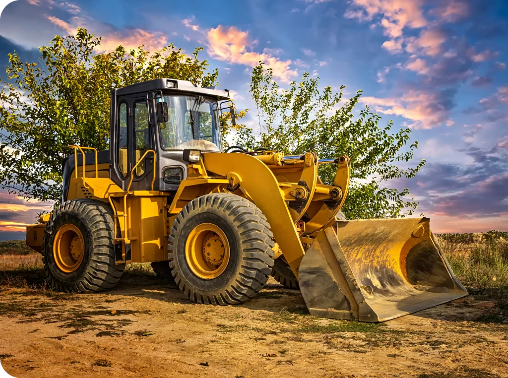 A yellow bulldozer with a large front bucket is parked on a dirt road, with a tree and a colorful sunset sky in the background, all secured under comprehensive Plant and Equipment Insurance.