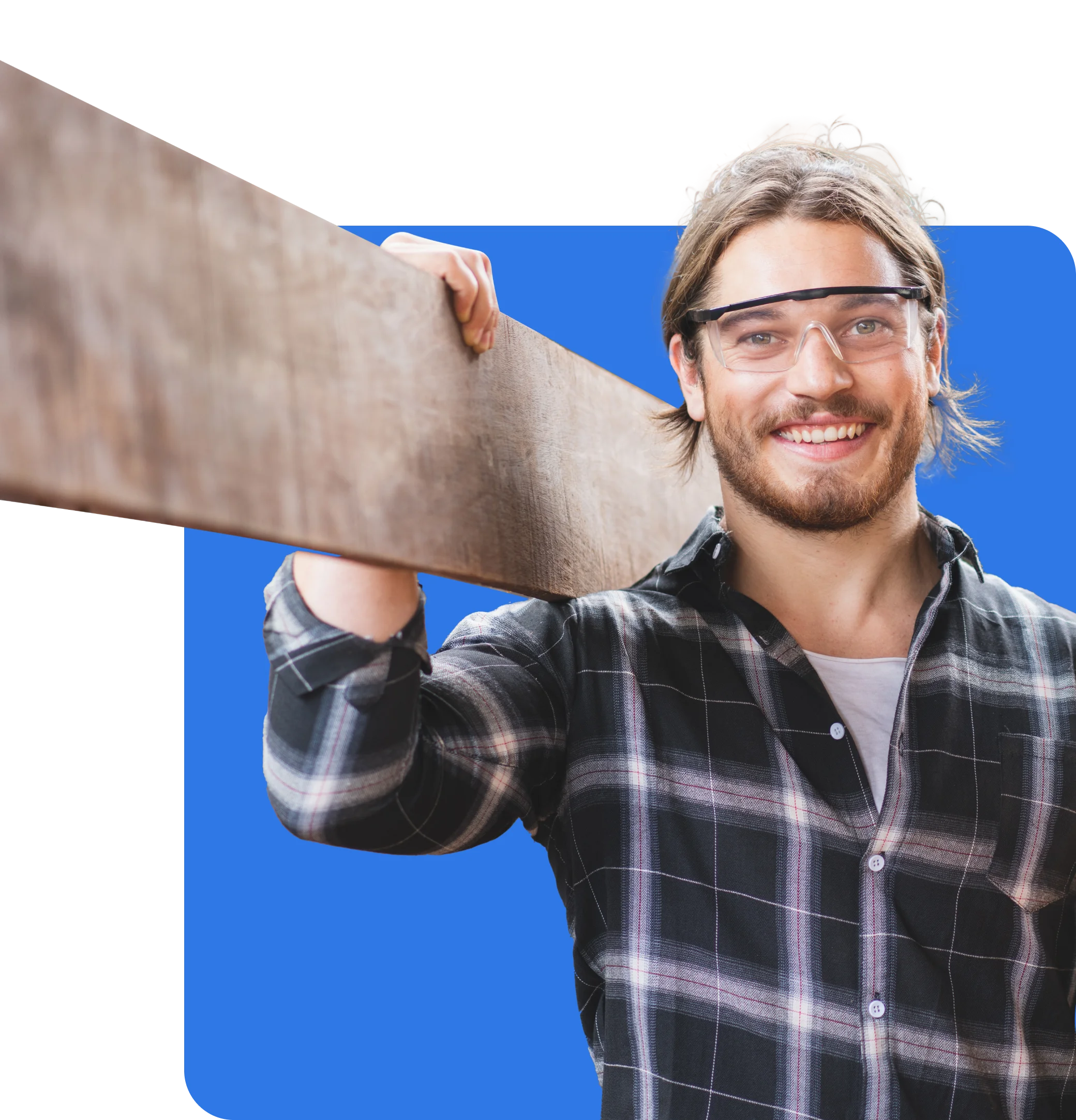 A person in safety glasses and a checkered shirt holds a wooden plank on their shoulder and smiles, confident in their work thanks to Carpenters Insurance.