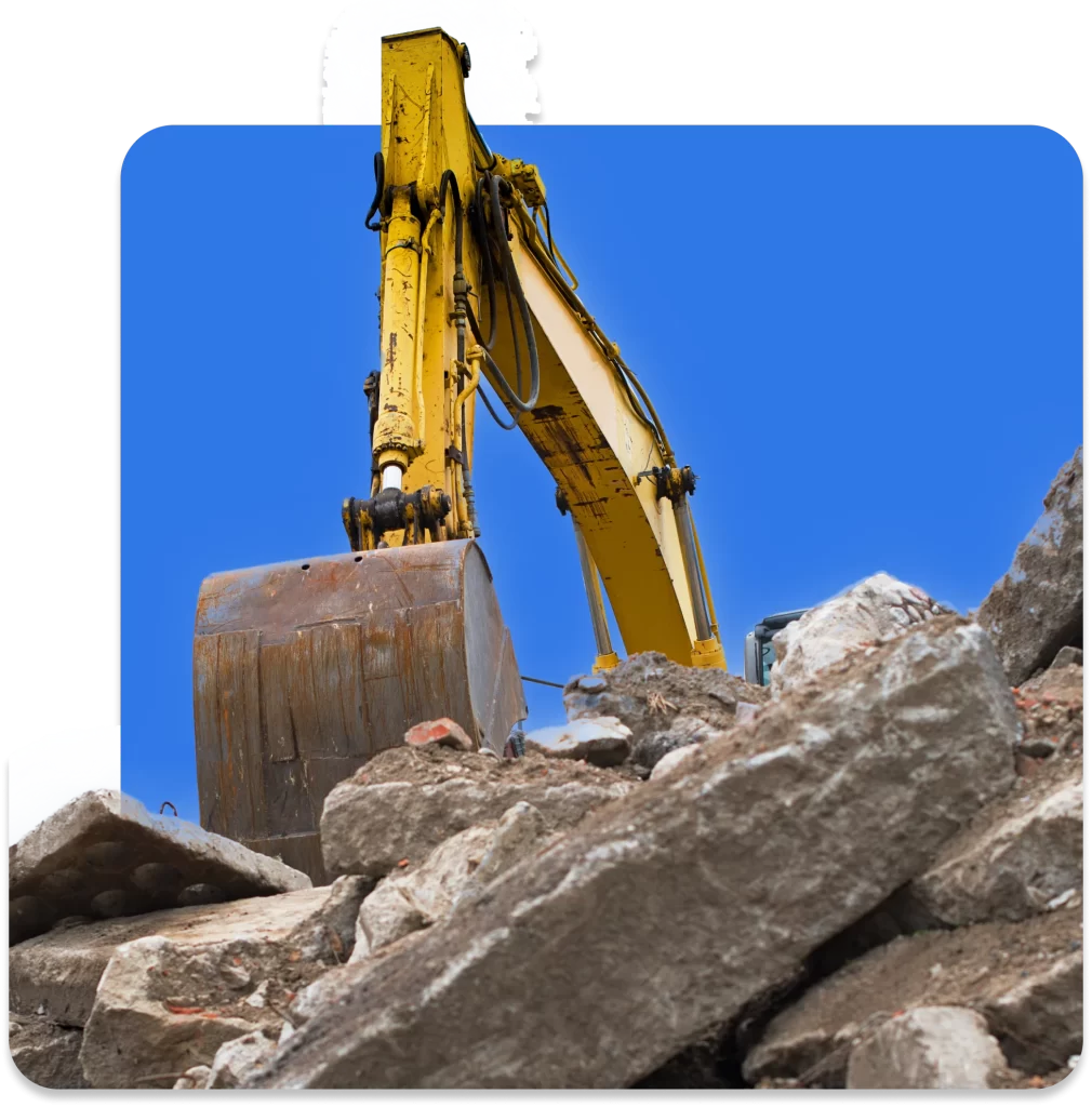 A yellow excavator with a large bucket is seen during the demolition of a structure, surrounded by rubble and debris, set against a clear blue sky—a prime example of why demolition insurance is essential for ongoing projects.