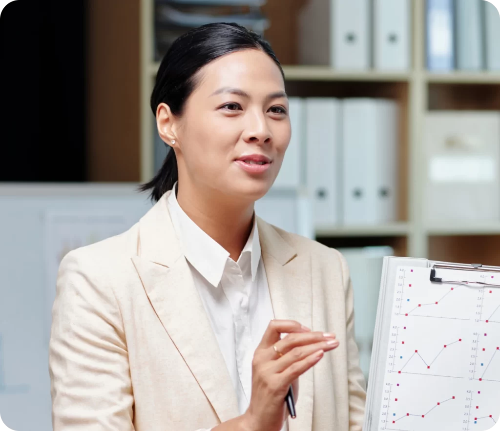 A person in a white blazer presents data on a clipboard in an office setting, emphasizing the importance of Professional Indemnity Insurance. Shelves with binders and documents are in the background, adding to the professional atmosphere.