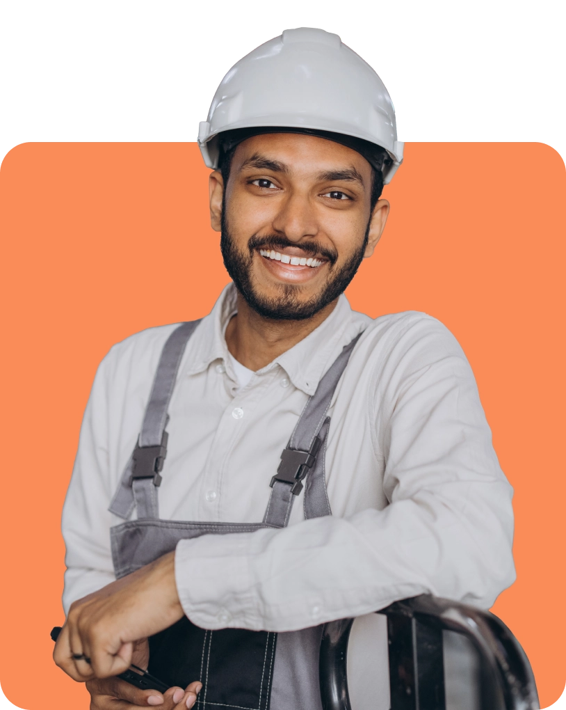 A person wearing a white hard hat and gray overalls, smiling in front of an orange background.