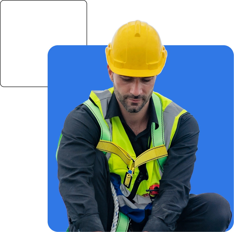 A man wearing a black shirt, yellow hard hat, and reflective safety vest works with a rope against a blue background, symbolizing the meticulous attention to detail that a business insurance broker brings to safeguarding your company's future.