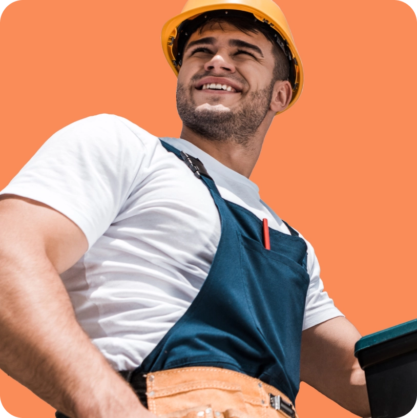 A man wearing a yellow hard hat, white shirt, and blue overalls stands outdoors, smiling and looking to the side against an orange background, perhaps contemplating the benefits of consulting with a business insurance broker.